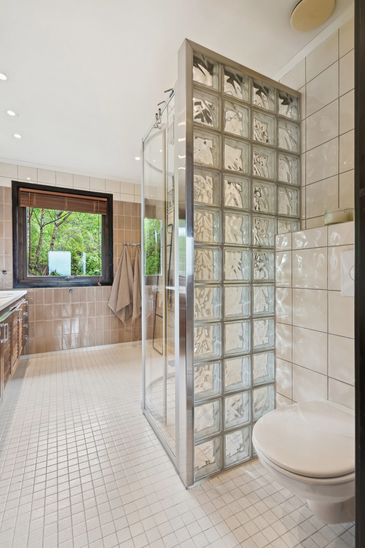 Dusjhjørnet har sort regnfallsdusj, skyvedører av glass og en vegg av glassbyggerstein mot toalettet. Galleribilde