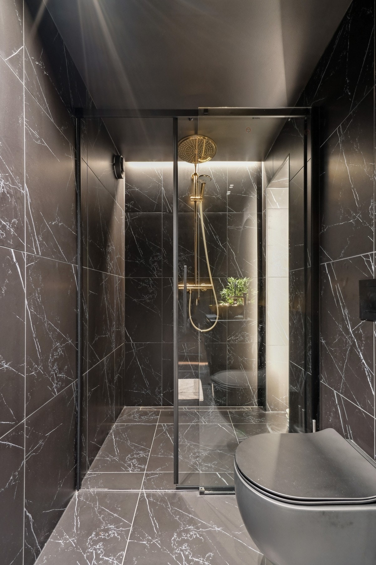 Et stort dusjhjørne har gullfarget regnfallsdusj, skyvedør av glass og et ekstra innhuk lyssatt med led-striper. Galleribilde