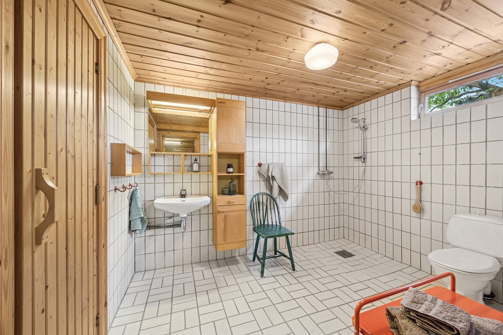 Badet er innredet med en enkel servant, speil med overliggende lys, toalett og dusj på gulv. Galleribilde