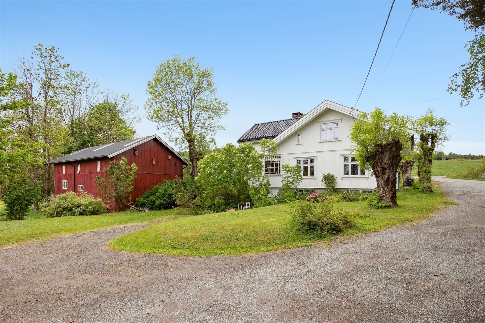 Den grusede gårdsplassen binder sammen hovedhus, låve og garasje i et helhetlig tun Galleribilde