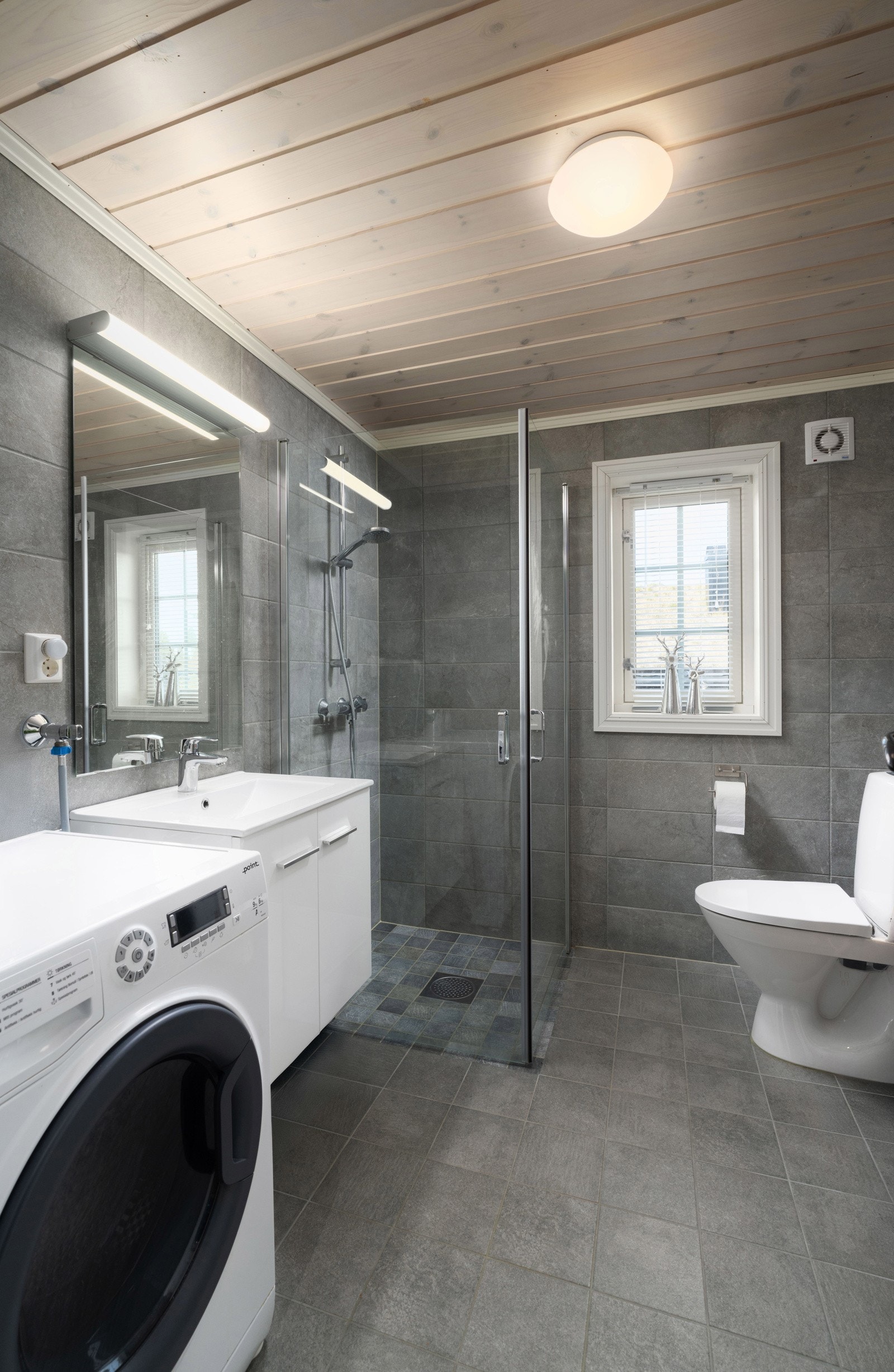 Hytta har ett bad i første etasje og et toalettrom på hemsen. Baderommet er stilrent og moderne, med grå fliser på vegg- og gulvflater. Galleribilde