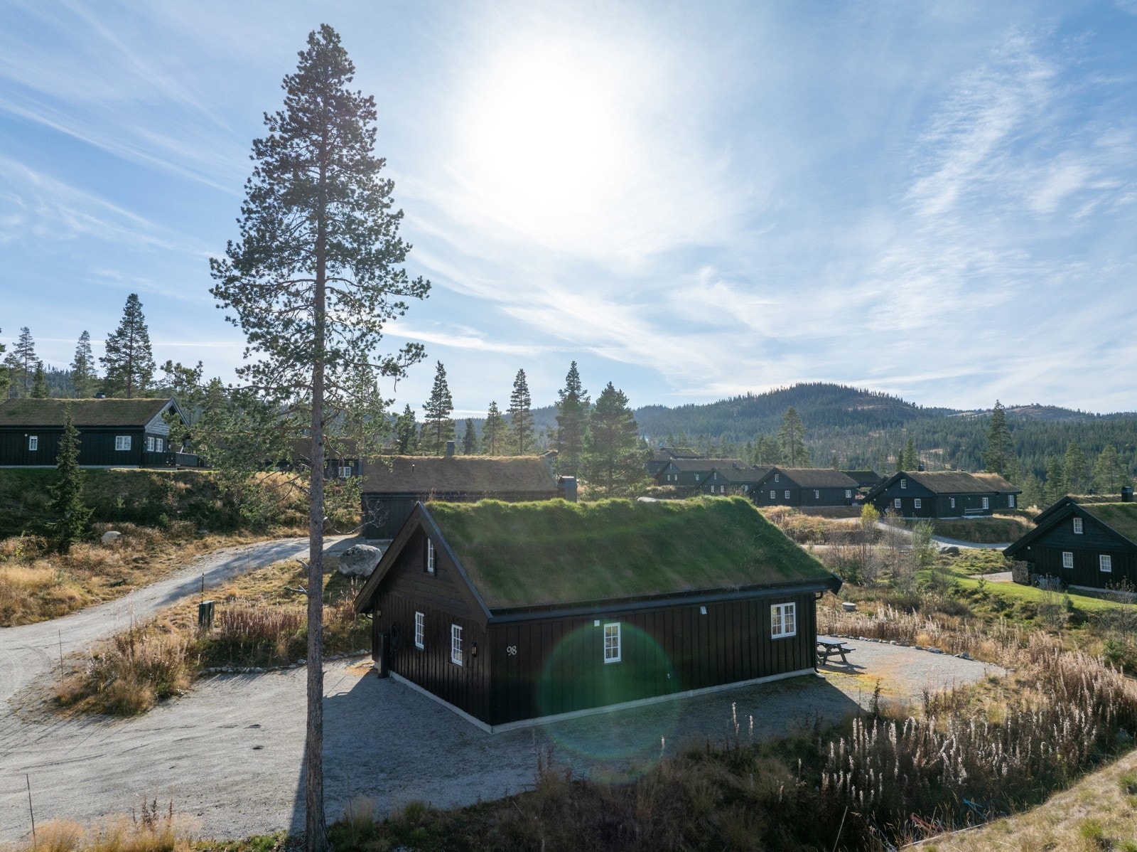 Hytta ligger åpent og solvendt til på en flat tomt hovedsakelig opparbeidet med grus. Galleribilde