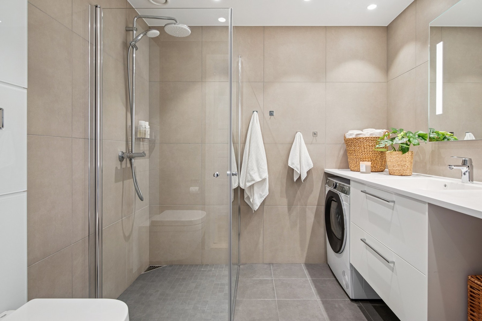 Baderommet er flislagt med store delikate fliser og utstyrt med servantinnredning og dusjhjørne med innfellbare glassdører. Galleribilde