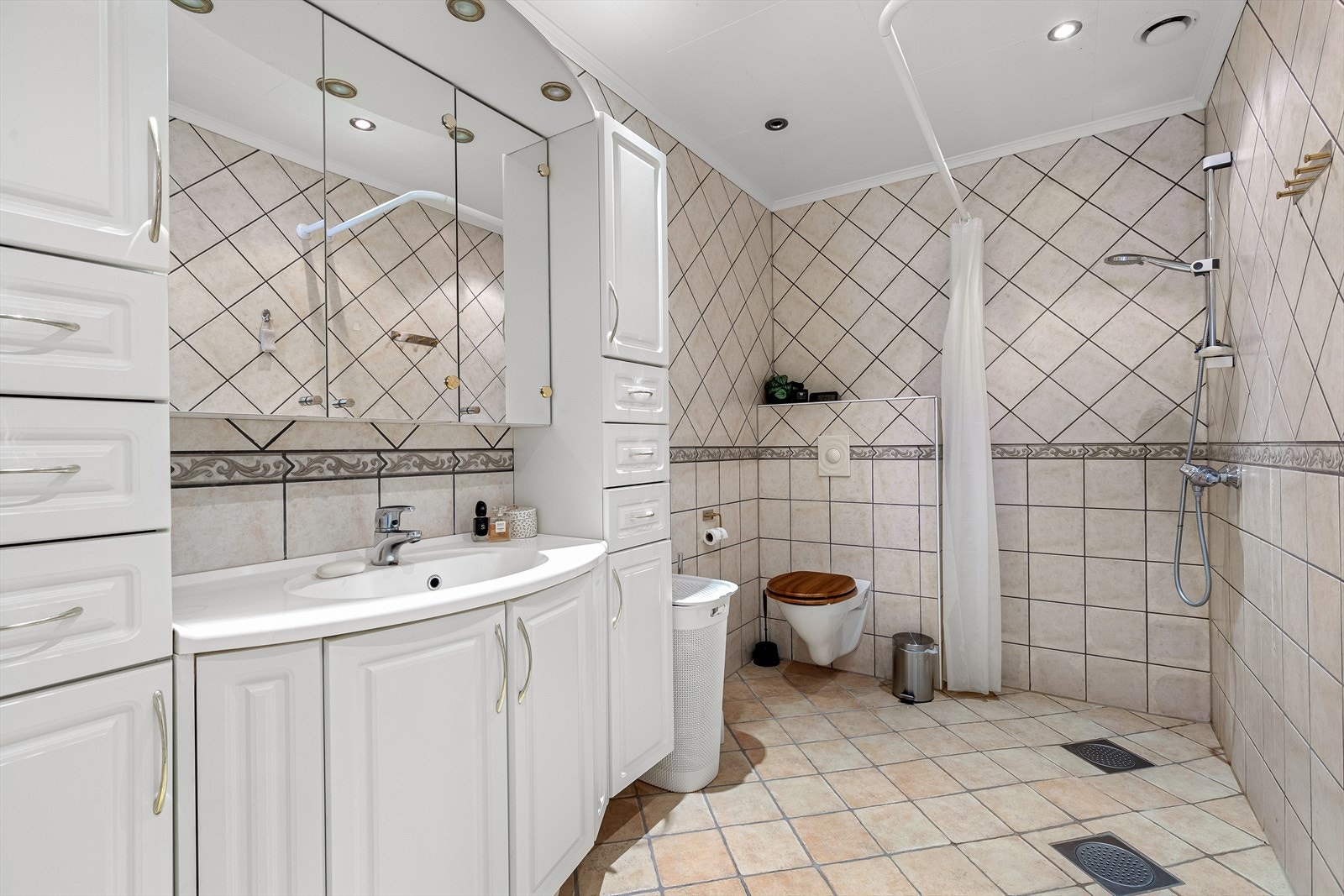 Heilflisa bad med varmekablar i golv. Badet er utstyrt med servant med innreiing, vegghengt toalett og dusj. Galleribilde