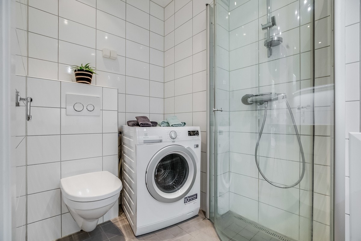 Badet inneholder dusjhjørne, servantinnredning med tilhørende møblement, servant med underskap og speil over, vegghengt toalett Galleribilde