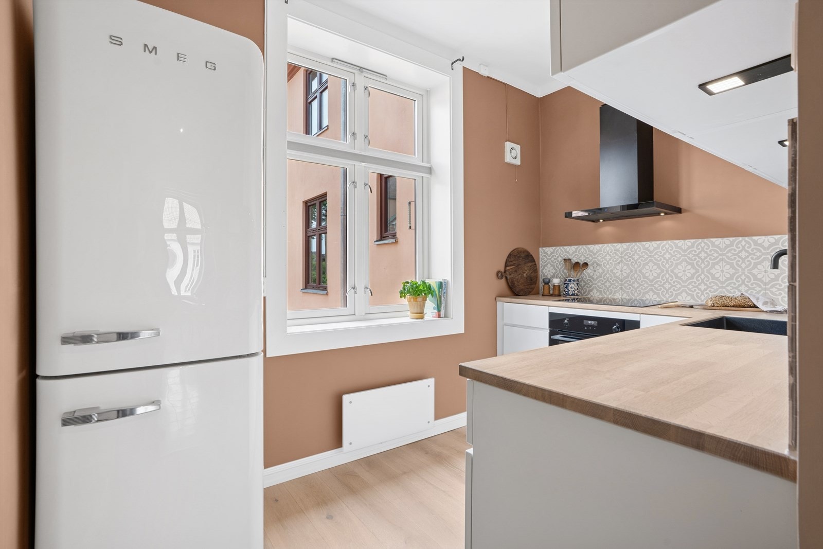 Det er lagt moderne fliser mellom overskap og benkeplate i tre. Kjøkkenet har integrerte hvitevarer som koketopp, ovn og oppvaskmaskin. Vifte med kullfilter. Kjøleskap medfølger ikke. Galleribilde