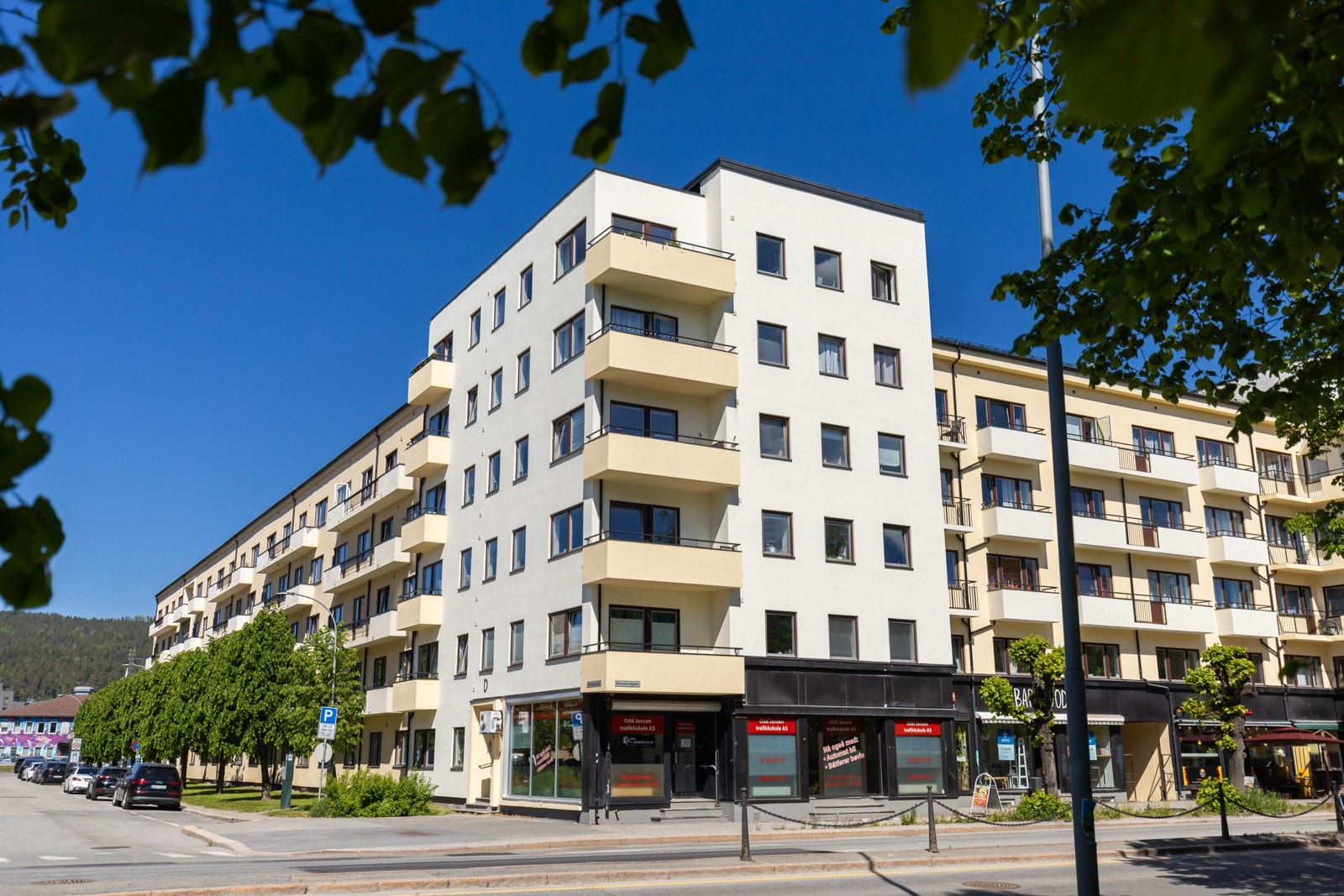 Moderne bygård med flere etasjer, balkonger og næringslokaler i første etasje. Lys fasade og god beliggenhet. Galleribilde