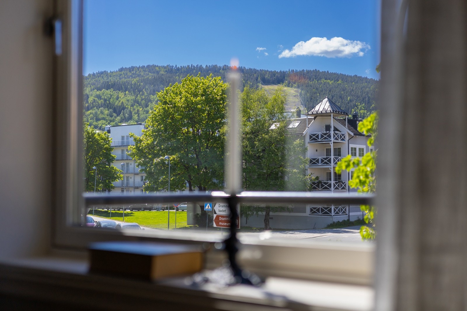 Utsikt fra vinduet mot grønne trær og en skogkledd ås i bakgrunnen. Galleribilde