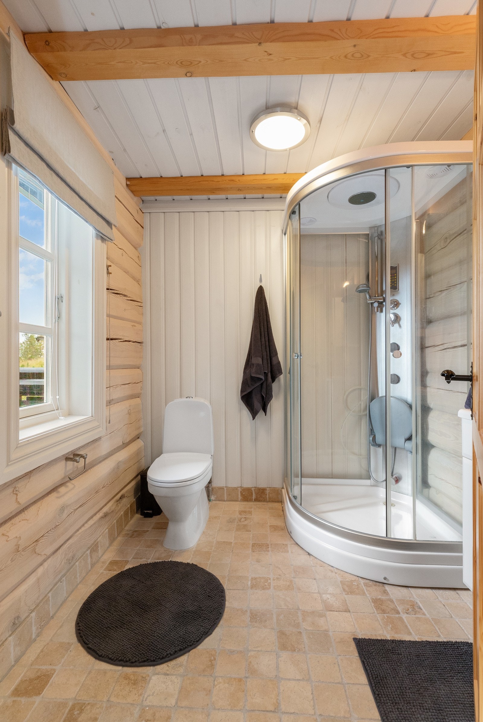 Badet i første etasje har flislagt gulv og synlige tømmervegger, samt en vegg med panel Galleribilde