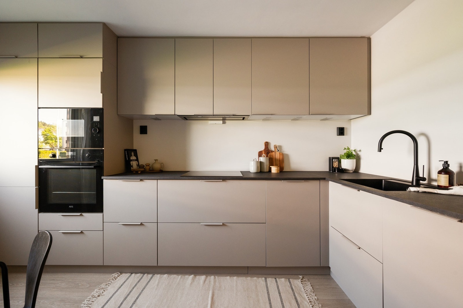 Kjøkkeninnredning med glatte fronter og laminat benkeplate med nedfelt vaskekum. Av integrerte hvitevarer er det integrert platetopp, micro, stekeovn, oppvaskmaskin og kjøl/frys. Hvitevarene er fra AEG. Opplegg for vaskemaskin. Galleribilde