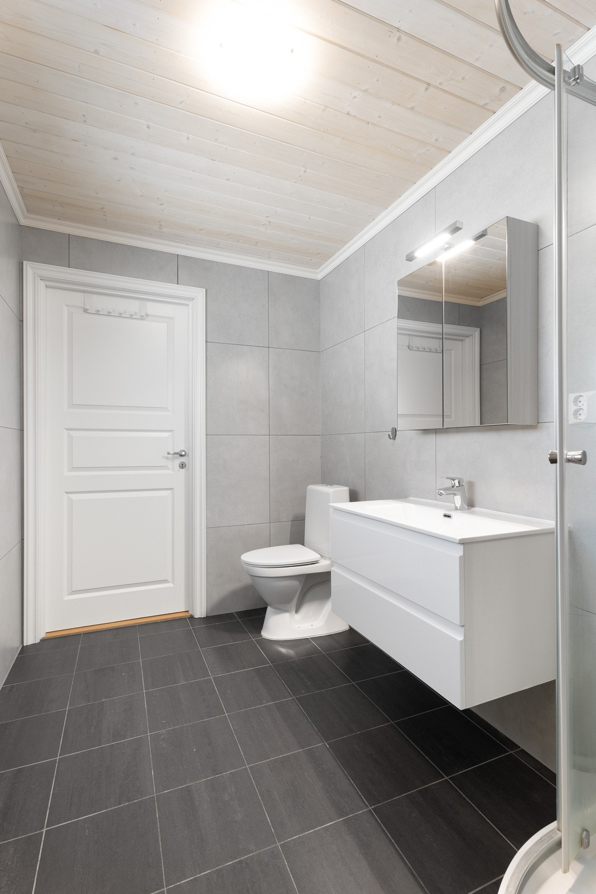 Moderne baderom med flislagt gulv. Baderommet inneholder toalett, dusjkabinett, innredning med servant og opplegg til vaskemaskin. Galleribilde