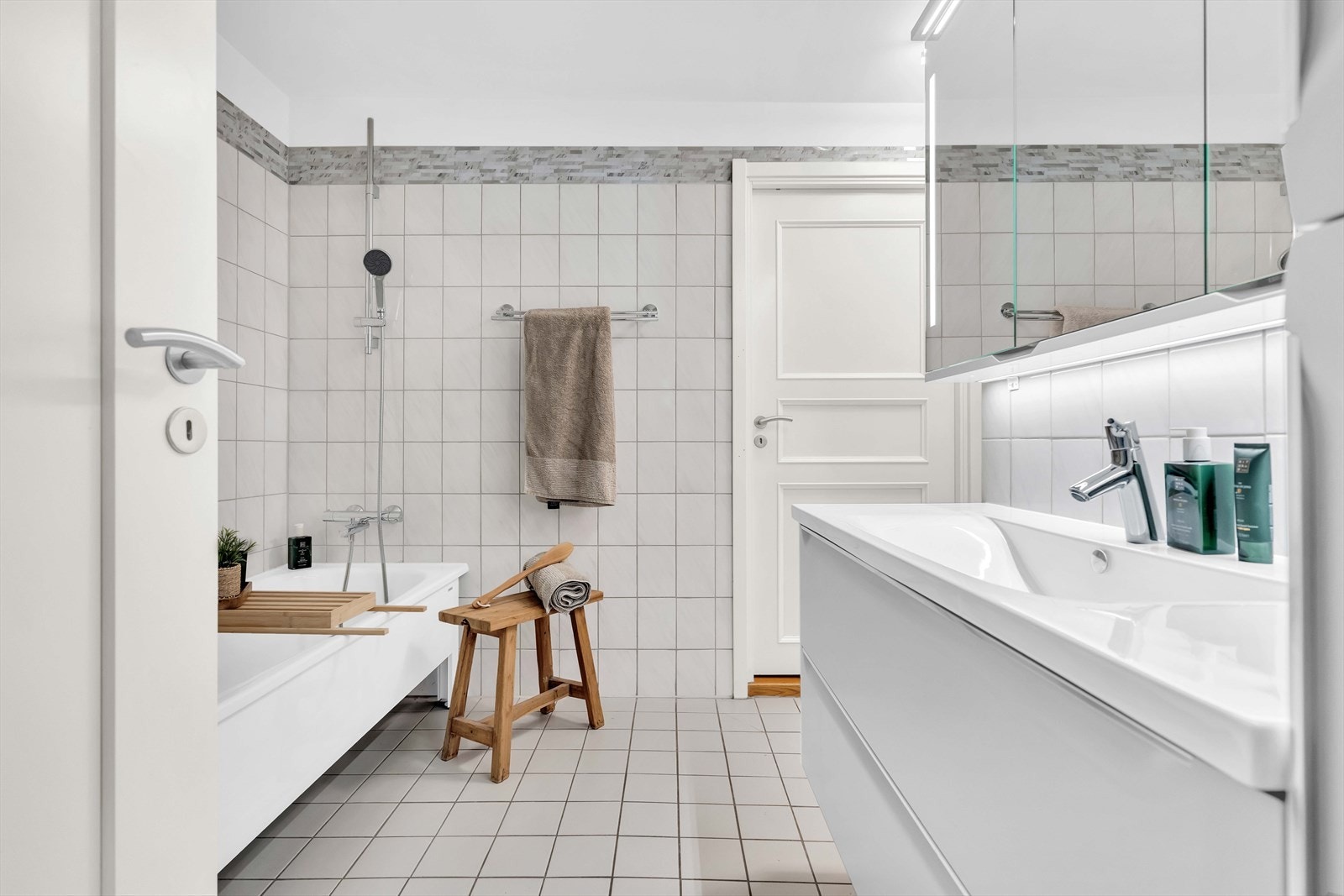 Rommet har flislagte gulv og vegger, varmekabler, speil med belysning og servant med slette fronter. Galleribilde