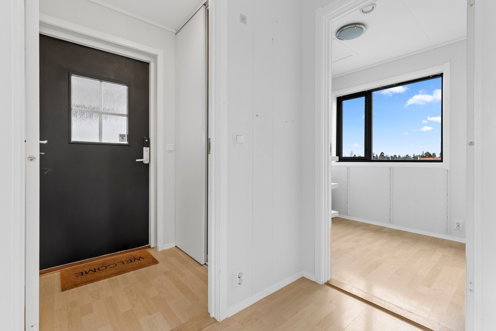 Tiltalende entre med laminat på gulv og lysmalte veggflater. Det er satt inn en skyvedørsgarderobe i vegg, perfekt til oppbevaring av yttertøy og sko. Galleribilde
