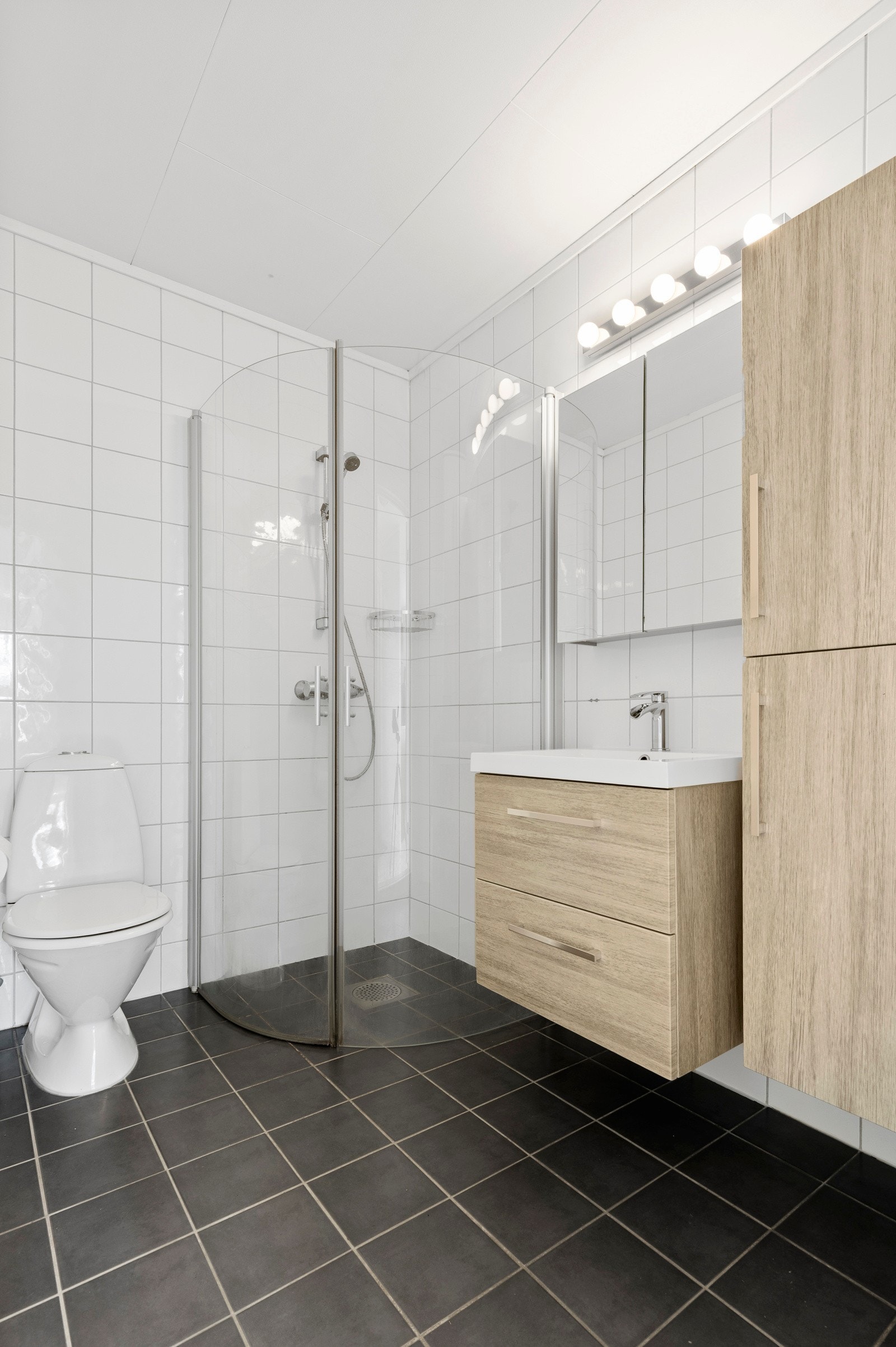 Pent bad med flislagte overflater og varmekabler i gulv, fra byggeår. Baderomsinnredningen består av stilrent servantmøblement med 2 skuffer, tilhørende speilskap m/toppmontert belysning, samt høyskap i samme utførelse. Galleribilde