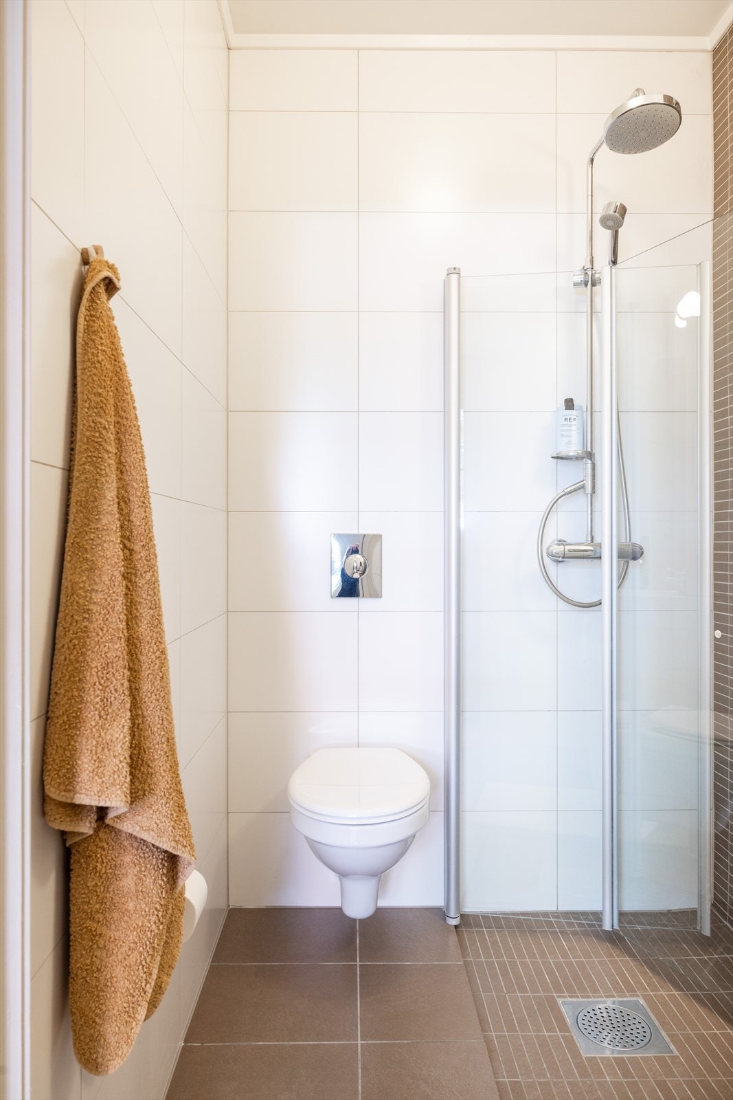 Badet er innredet med vegghengt toalett, servant med innredning og dusjhjørne med innfellbare glassdører. Galleribilde