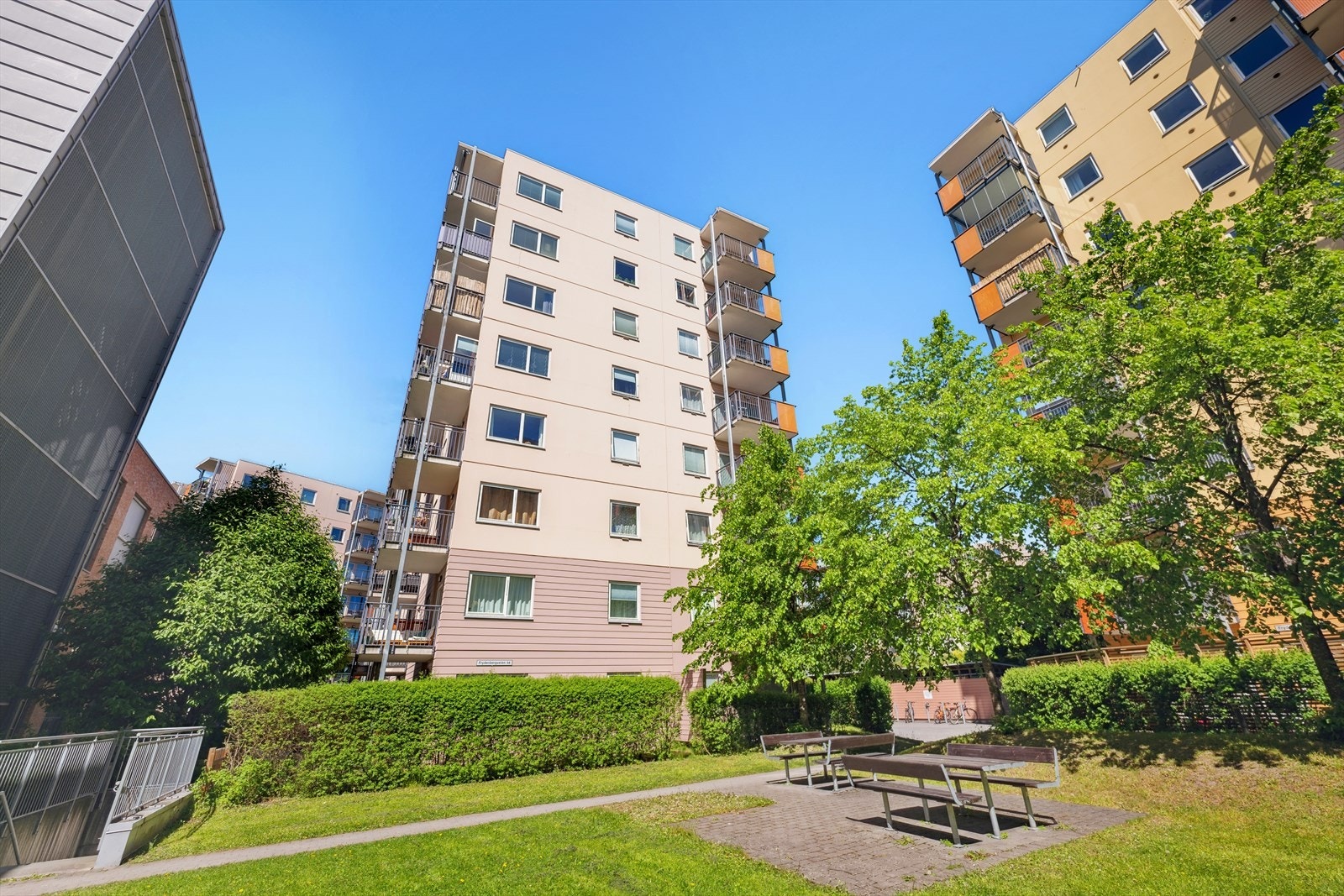 Fasadebilde av bygget. Tomten er pent opparbeidet med grøntområder, beplantning og sitteplasser Galleribilde