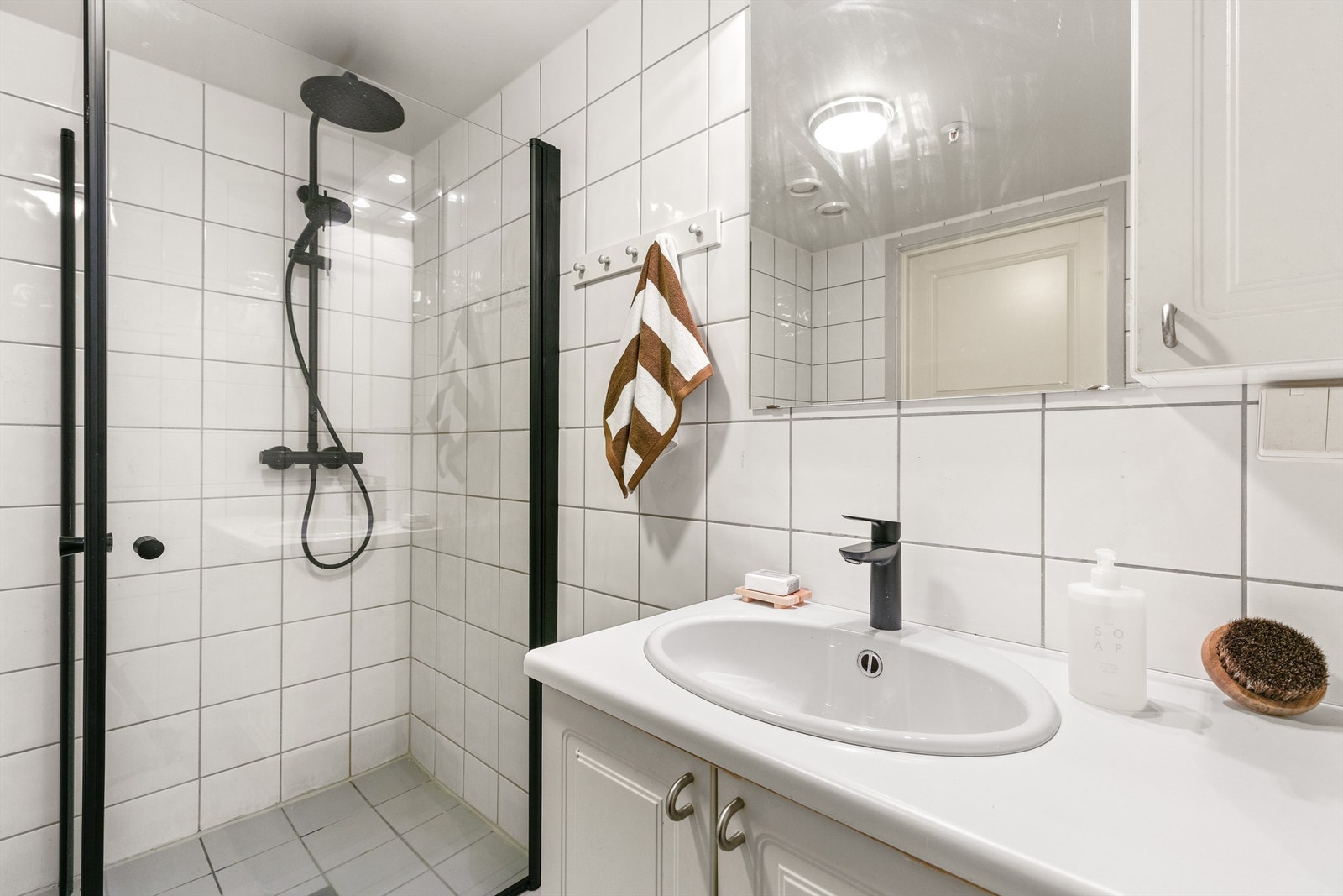 Videre har badet en vegghengt servantinnredning med laminert benkeplate og nedfelt servant med ett-greps armatur. Speil på vegg med overlys samt stikkontakt. Vegghengt skap for oppbevaring. Galleribilde