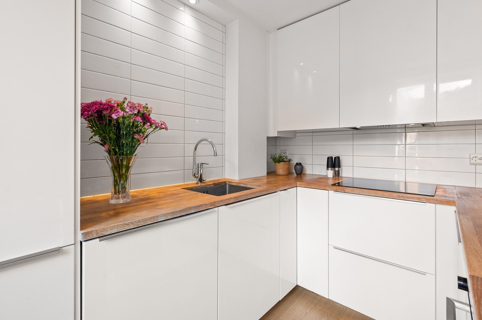 Kjøkkenet er utstyrt med takhøye overskap som gir ekstra lagringsplass. Integrerte hvitevarer inkluderer induksjonstopp, stekeovn, oppvaskmaskin og kombinert kjøl/frys Galleribilde