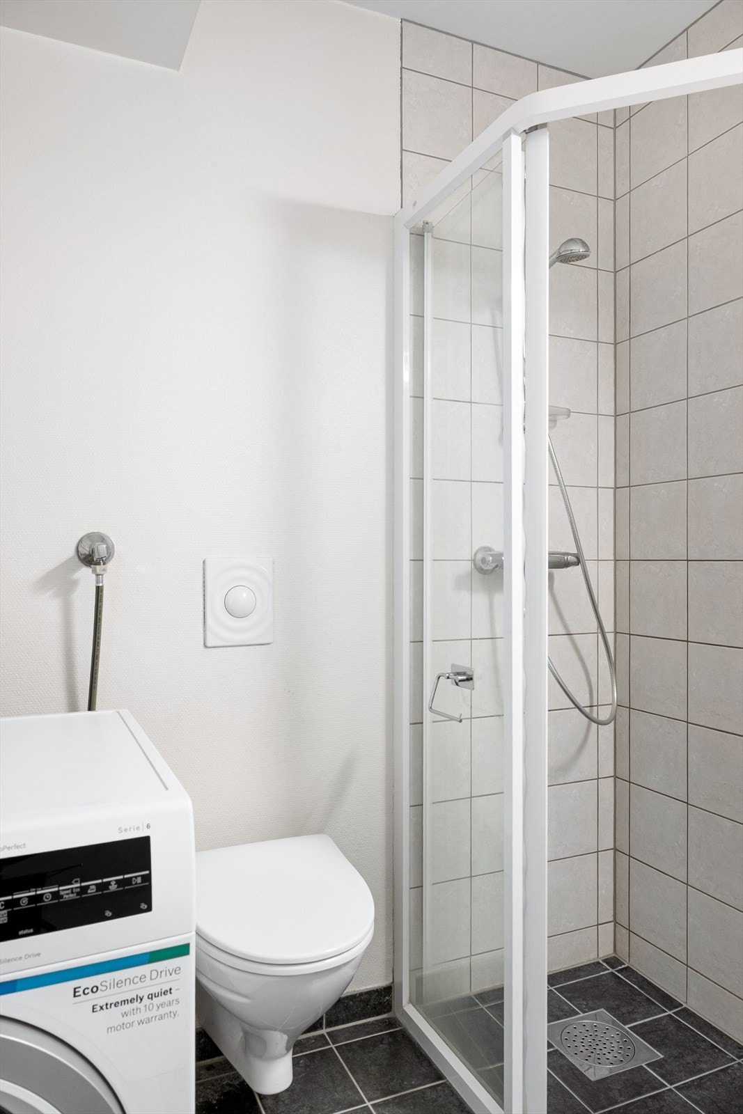 Innredet med servant i baderomsmøbel, vegghengt toalett og dusjhjørne. Videre har badet opplegg for vaskemaskin. Galleribilde