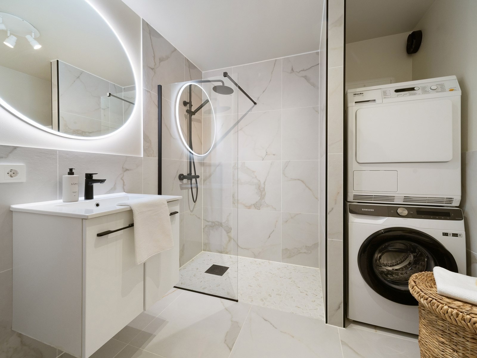 Badet har varmekabler i gulvet og er utstyrt med veggmontert toalett, dusj, servant i møbel, speil med lys, samt opplegg for vaskemaskin som er praktisk plassert i en egen nisje. Galleribilde