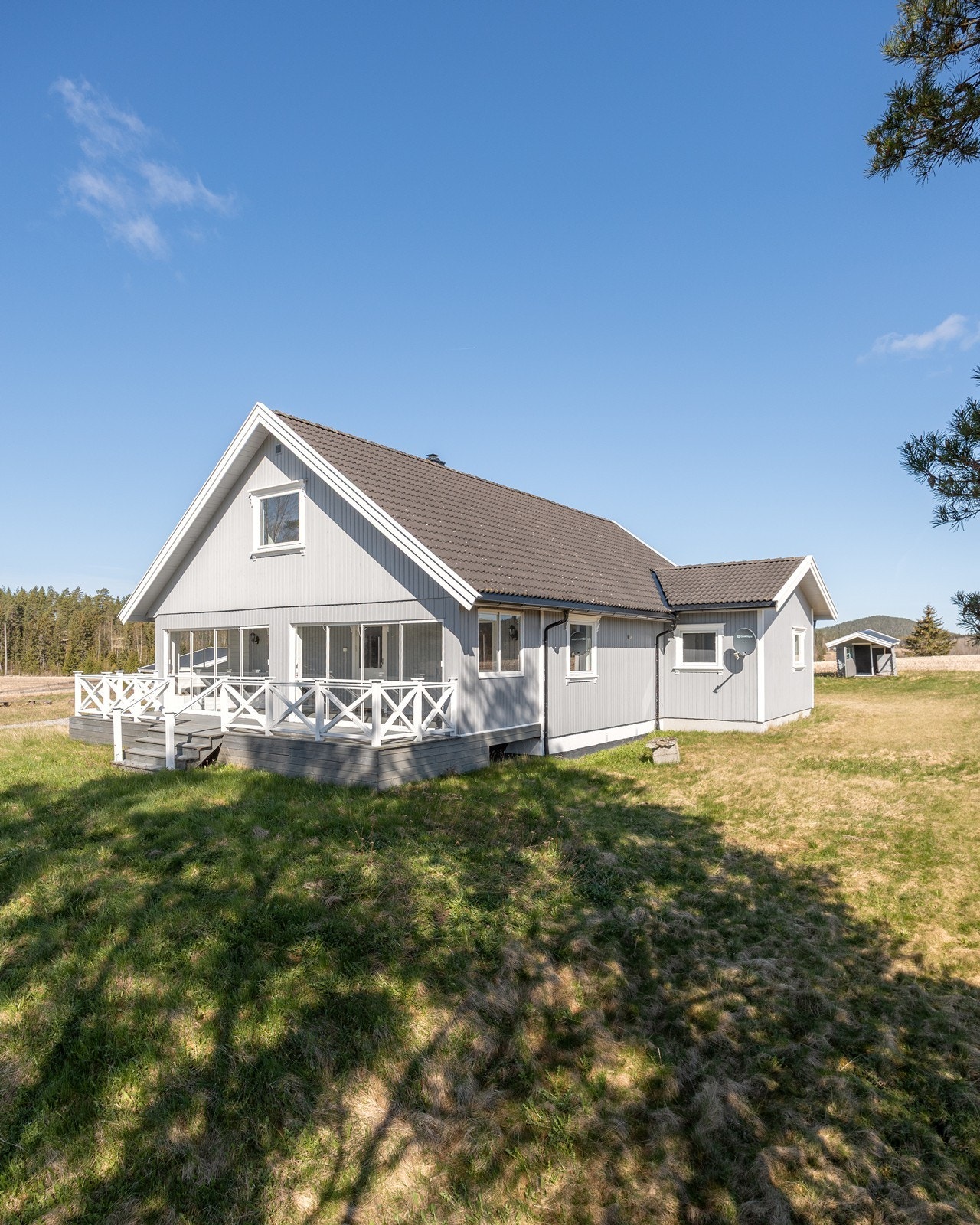 Tomten er solrik med grønt hageareal, noen treklynger, hekk og gruset gårdsplass. Galleribilde