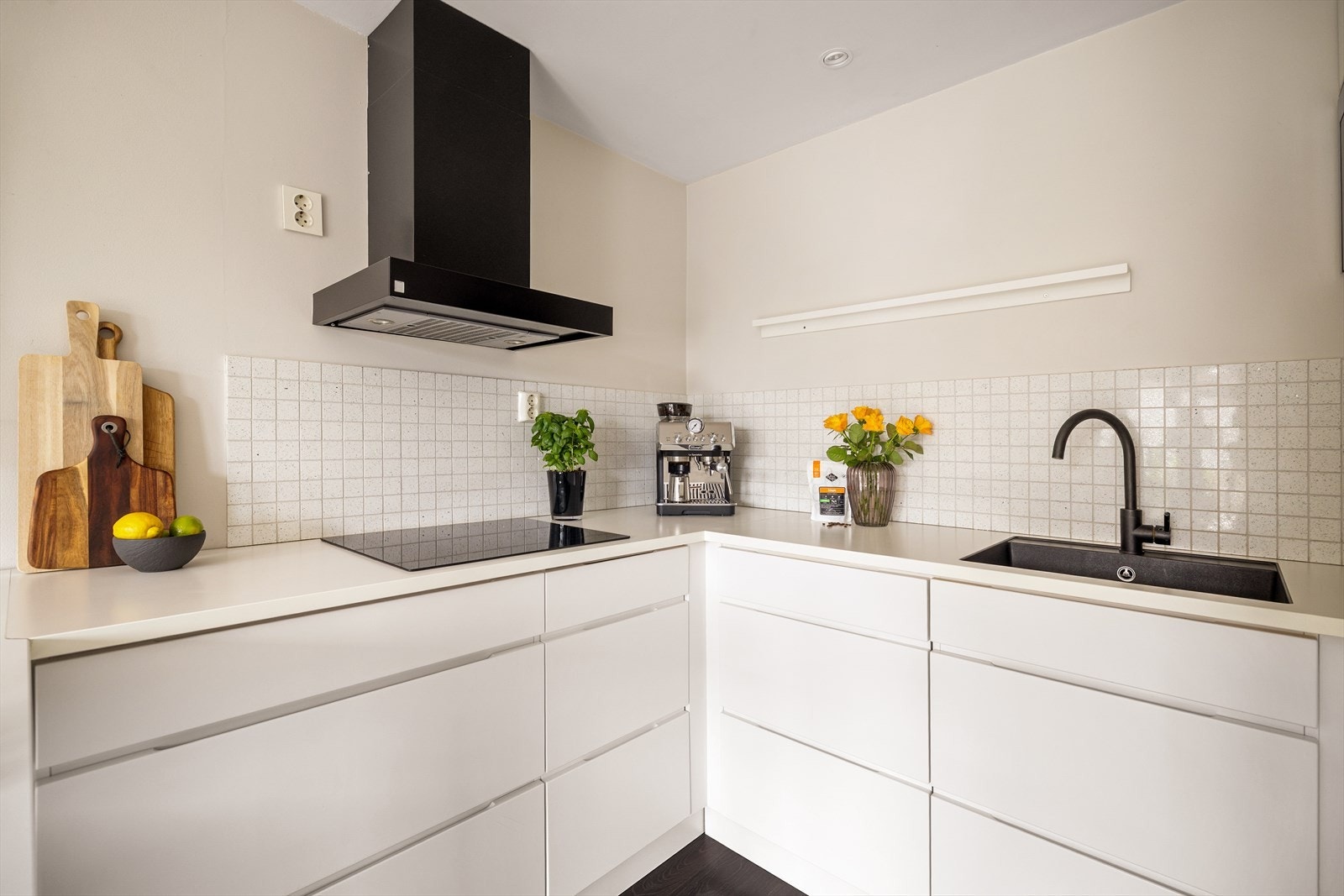 Lys innredning med glatte fronter, fliser på vegg over kjøkkenbenk og benkeplate i laminat. Kjøkkenet er utstyrt med integrerte hvitevarer som består av koketopp, ovn, mikro og oppvaskmaskin. Galleribilde