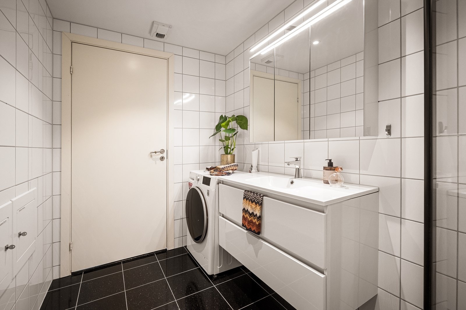 Rommet inneholder gulvstående toalett, dusjhjørne med innfellbare glassdører og baderomsinnredning med servant, ettgreps blandebatteri, skuffer og vegghengt speilskap med belysning. Galleribilde