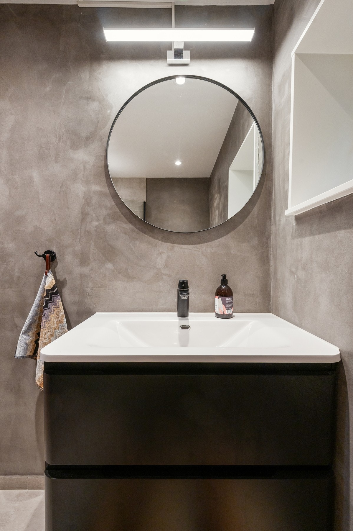 Badet har grå vegger, svart servantskap, rund speil og enkel belysning. Galleribilde