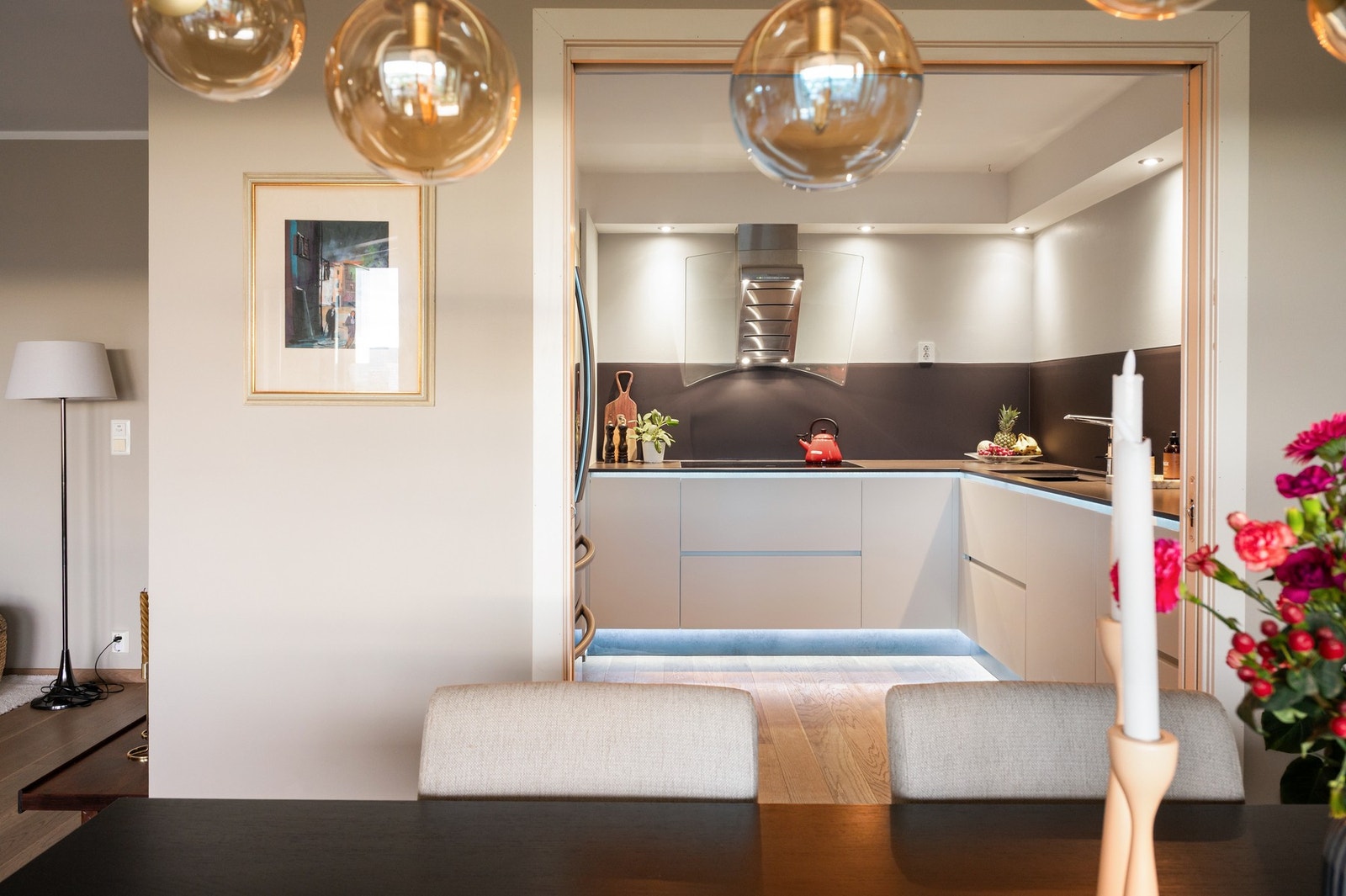 Moderne kjøkken med innebygd ventilator og hvite skap. Lys grå vegger og belysning under skapene. Galleribilde