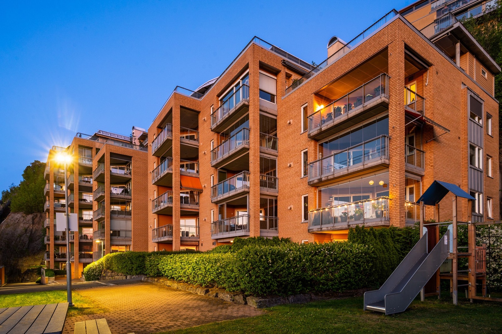 Moderne leilighetskompleks i murstein, med balkonger og lekeplass, omkranset av grøntområder. Galleribilde