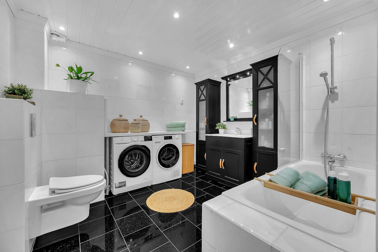 Nisje til vaskemaskin og tørketrommel på bad. Badekar med vegghengt badekararmatur. Galleribilde