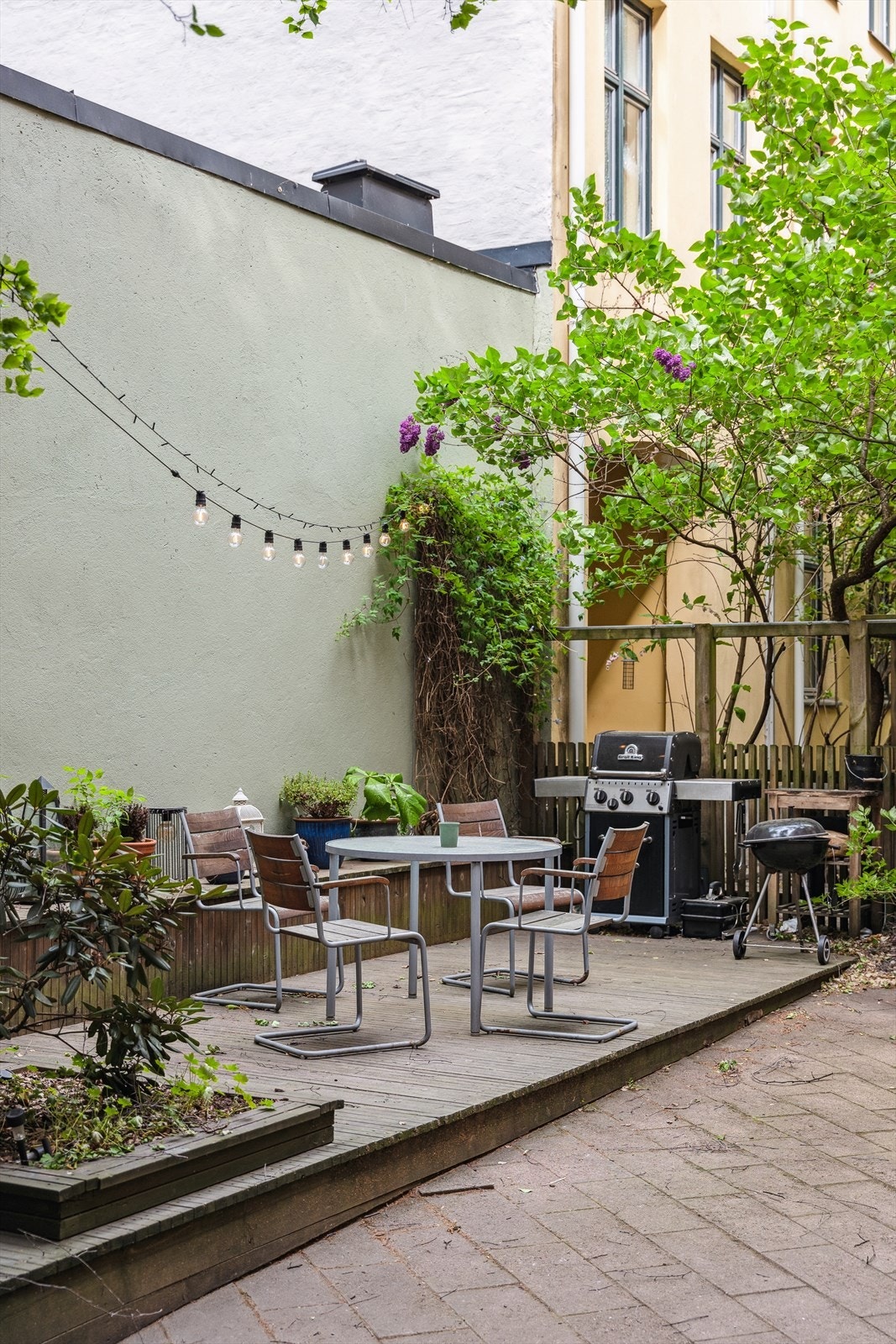 Hyggelig bakgård med sittegrupper, grill, beplanting og lyslenker. Galleribilde