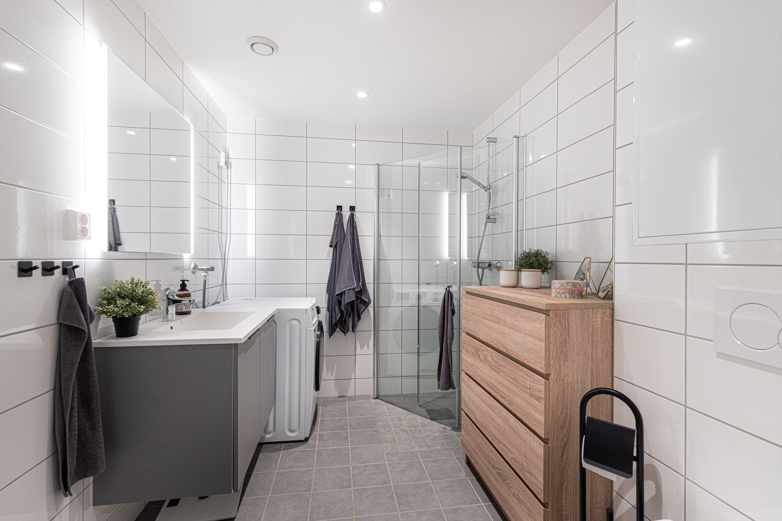 Det delikate badet er helfliset med vannbåren varme i gulvet. Her er det innredning i samme utførelse som kjøkkenet, med heldekkende servant og speil med belysning. Galleribilde