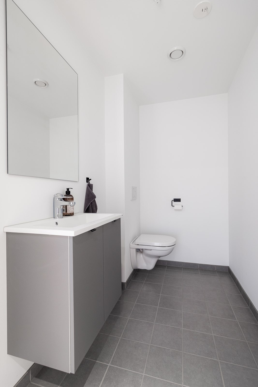 Leiligheten har eget gjestetoalett i gangen, med flislagt gulv og slette, malte gipsplater på veggoverflatene. Toalettrommet er innredet med servantskap, speil og veggmontert toalett. Galleribilde