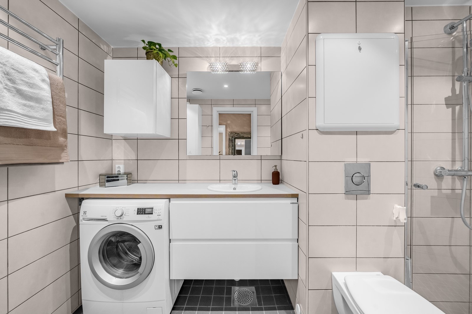 Pent baderom fra 2021 med flislagte overflater, moderne innredning og opplegg for vaskemaskin. Galleribilde
