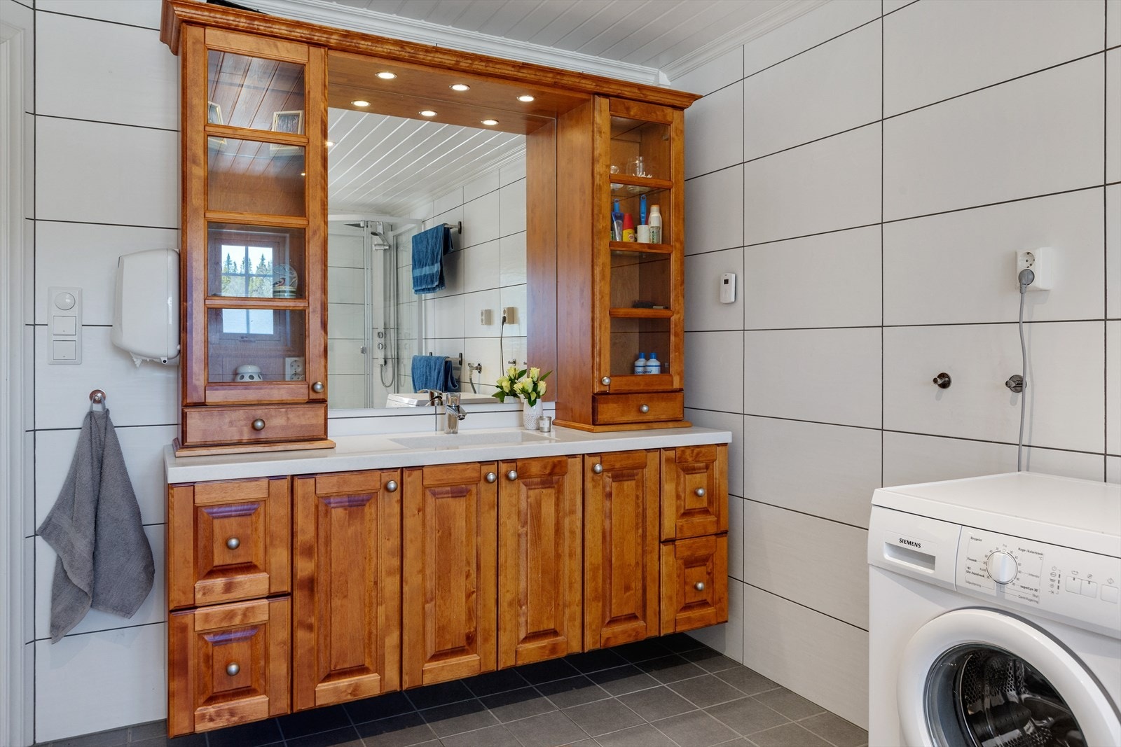 Baderomsinnredning med over og underskap og hel benkeplate med servant og kran av stål, speil med tilhørende belysning. Galleribilde