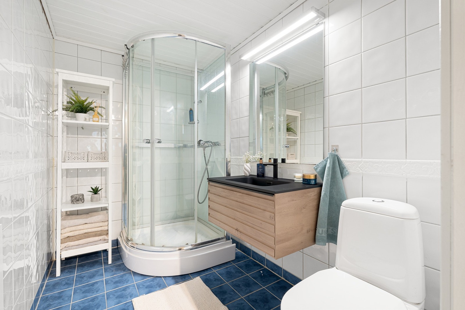 Lyst og innbydende bad med dusjkabinett, vegghengt servantinnredning og praktisk oppbevaringsplass. Galleribilde