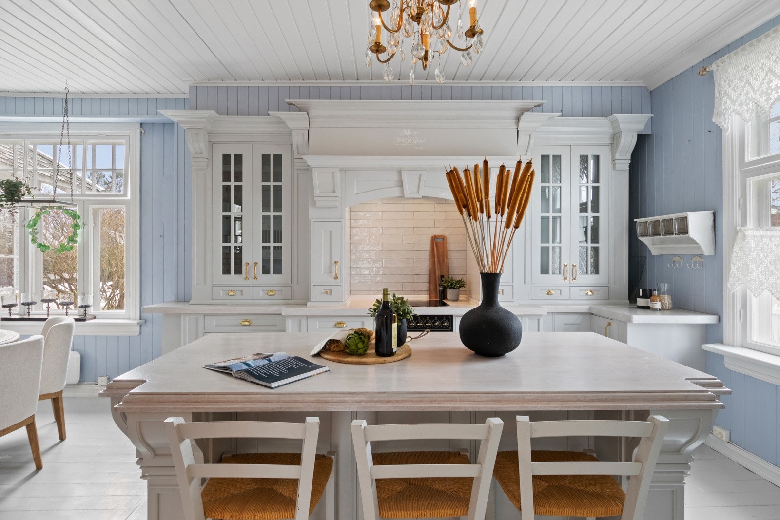 Store T-postvinduer bidrar med mye naturlig lys, og kjøkkenet har malt tregulv med varme, god plass til spisebord og panelvegger holdt i en nydelig pastellblå nyanse. Galleribilde