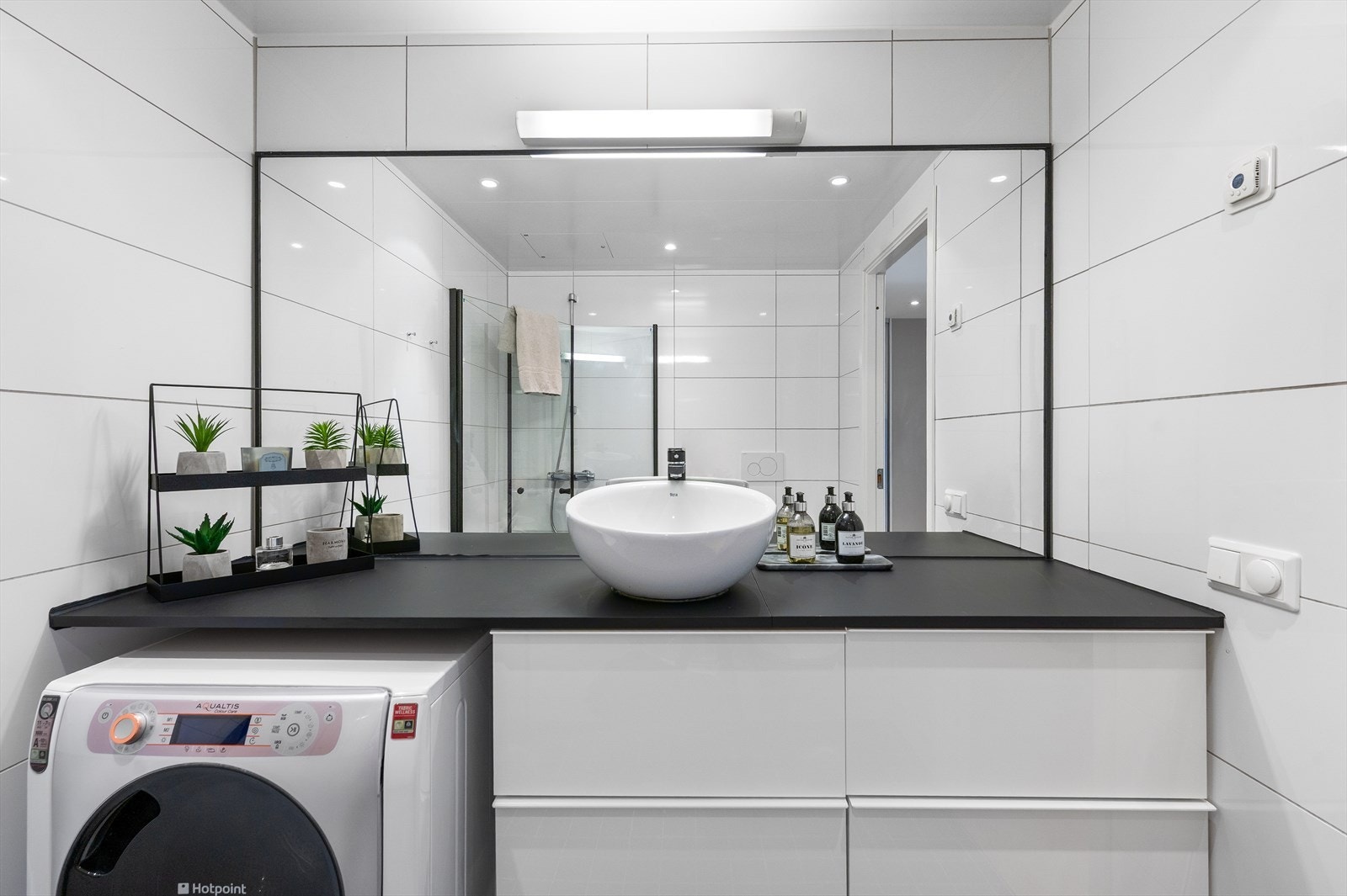 Rommet er innredet med vegghengt toalett, servant på benkeplate, nytt servantbatteri fra 2025, stort speil med belysning og dusjhjørne med svingbare glassdører. Galleribilde