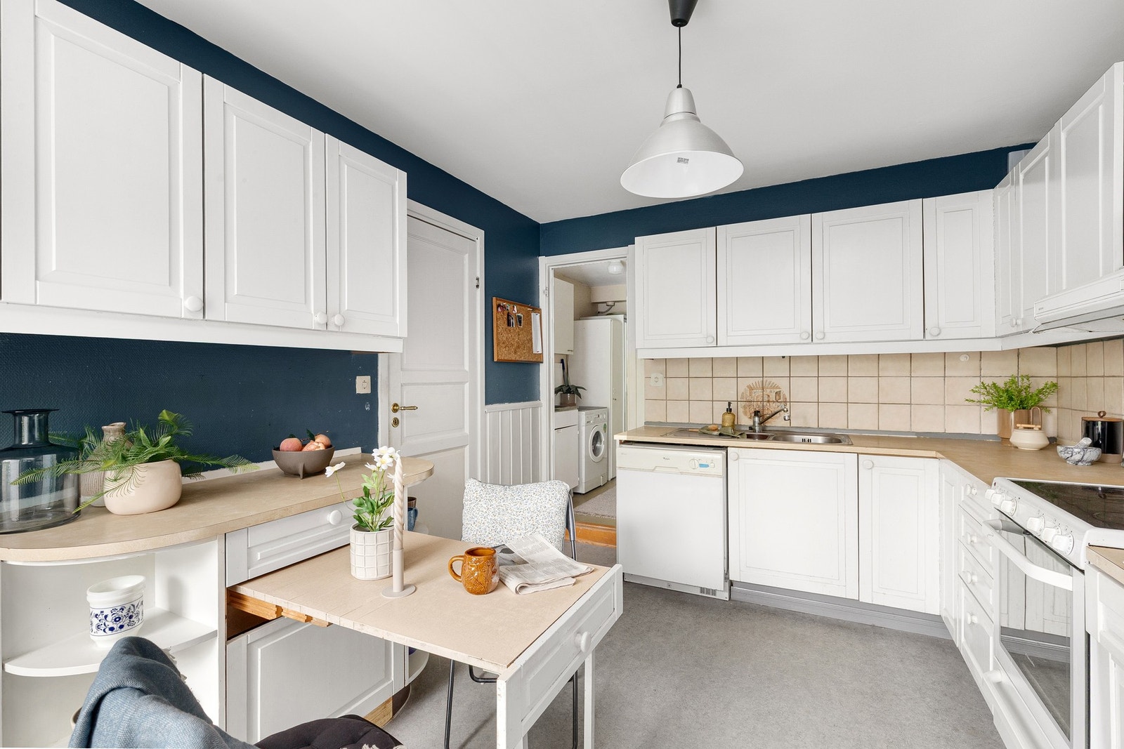 Kjøkkeninnredning med hvite, profilerte fronter, laminat benkeplater, fliser over benk og belysning under overskap Galleribilde