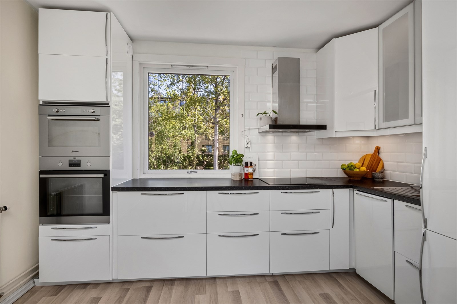 Delvis åpent kjøkkenløsning (2016) med glatte fronter og enkelte glassfronter i overskap. Induksjonstopp, stekeovn, oppvaskmaskin, mikrobølgeovn og kjøl/frys er integrert i innredningen. Galleribilde