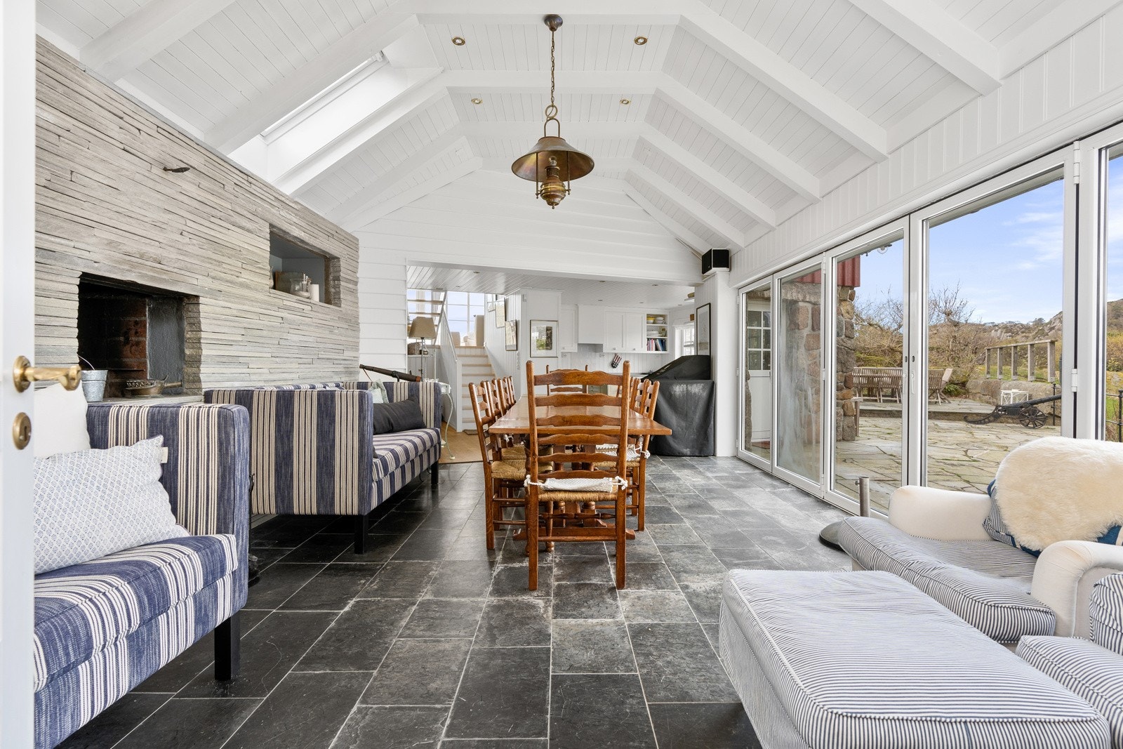 Romslig peisestue i 1.etg. med åpen himling og med skyvedører ut til skiferlagt platting Galleribilde