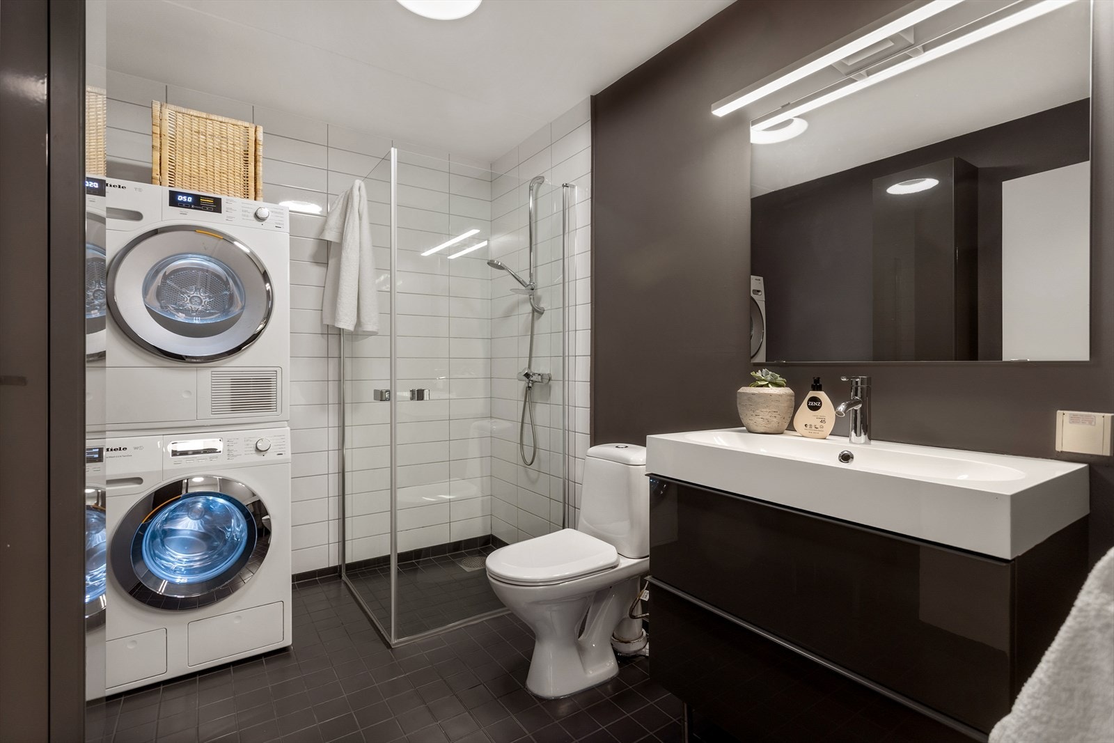 Badet er utstyrt med wc, servant med skuffer under, dusj i hjørne samt opplegg for vaskemaskin og tørketrommel. Galleribilde
