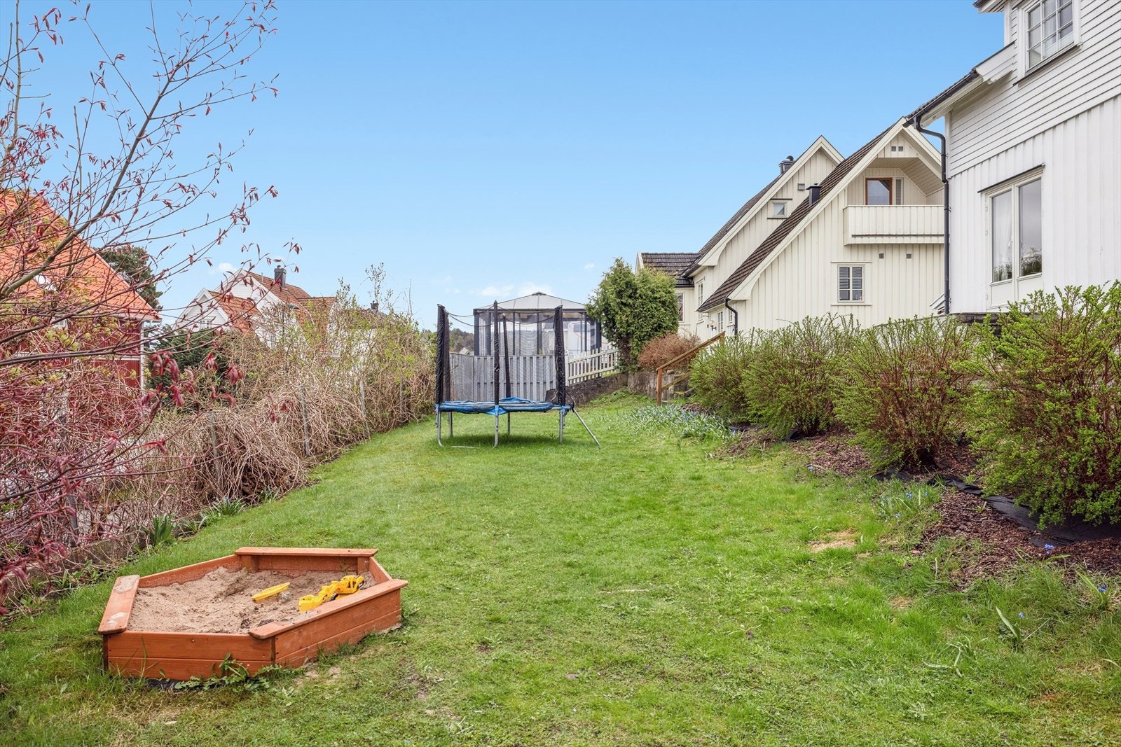 Koselig hage med lekeområde og trampoline, omgitt av grønne busker. Galleribilde