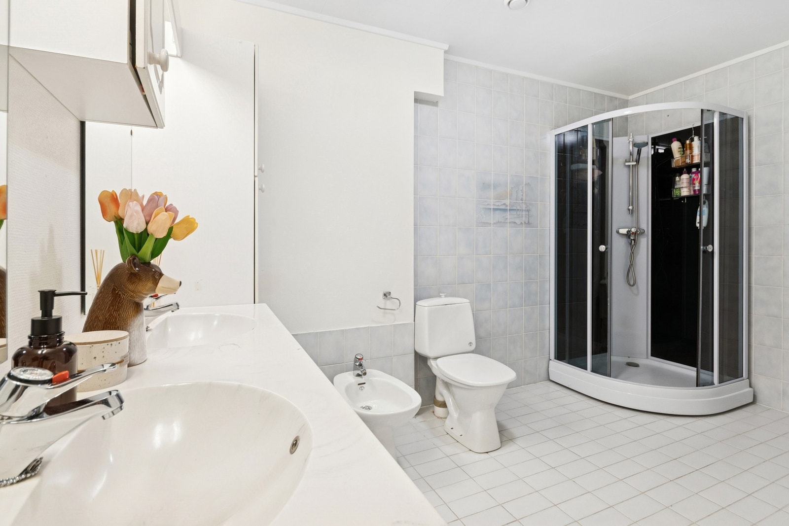 Badet i underetasjen har flislagt gulv og våtromsstrie på vegg. Innredning med to nedfelte servanter, dusjkabinett, toalett og bidé. Elektriske varmekabler i gulv. Galleribilde