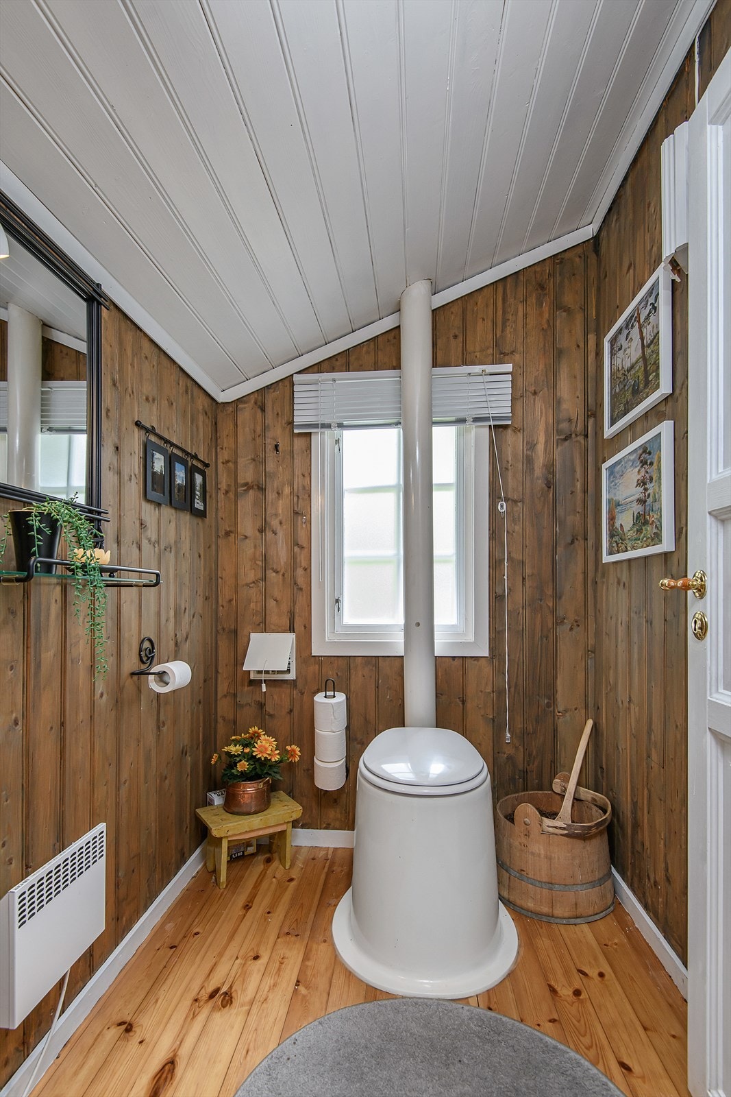 Toalettrom med tregulv og panelvegger. Innredningen består av gulvstående sanitærtoalett. Rommet har naturlig avtrekk og ventil på vegg. Galleribilde