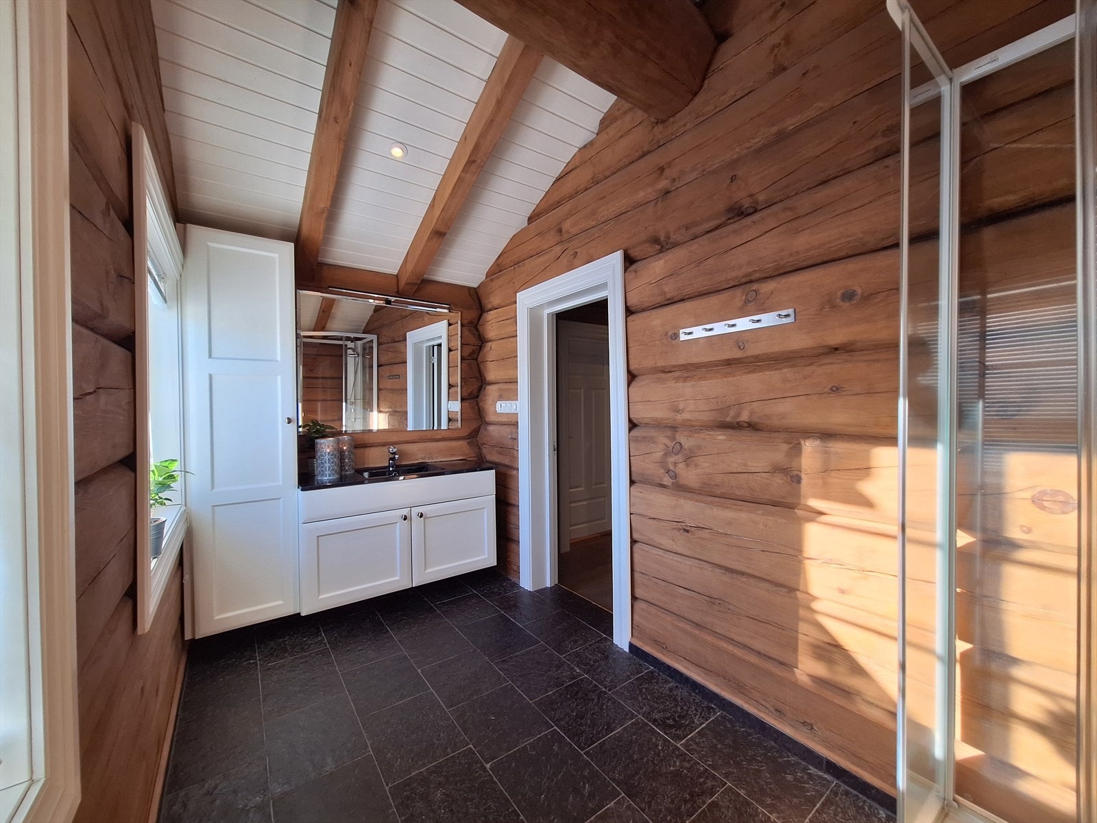 Stort bad i 2. etasje med fliser på gulv og varmekabler, beiset tømmer på vegger og malt trepanel og beiset dragere i himling. Galleribilde