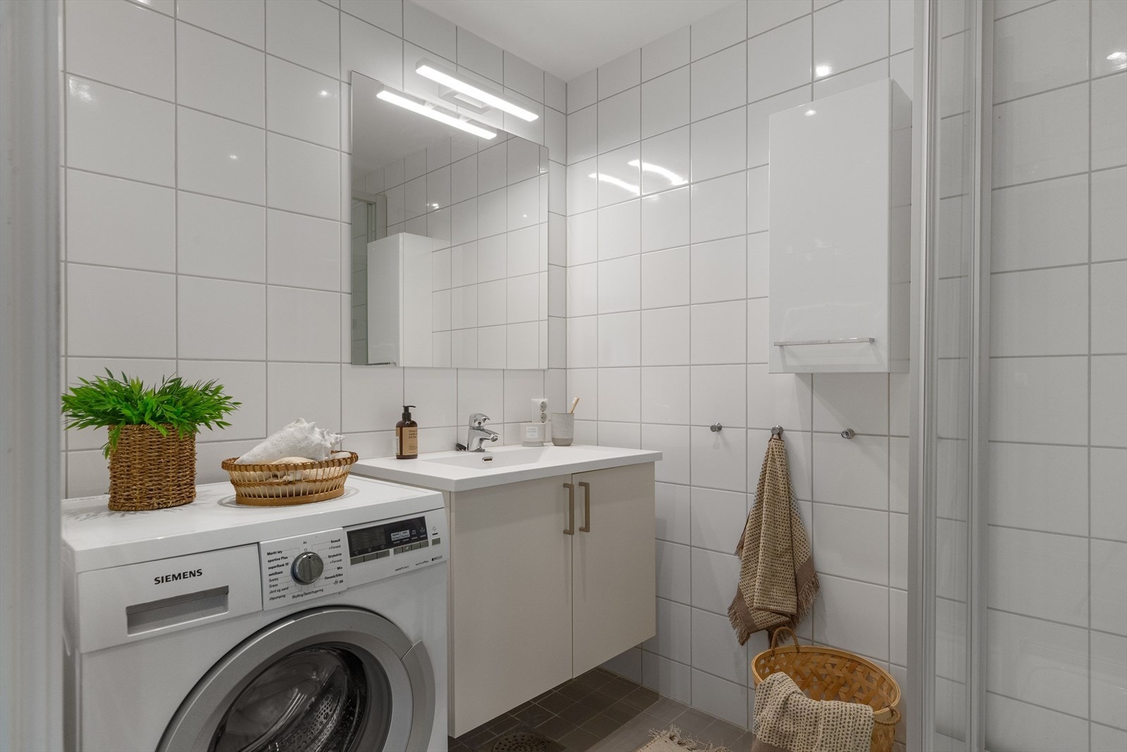 Baderommet er flislagt og har en moderne og ryddig innredning med dusjhjørne, vegghengt toalett og servant med skuffer. Galleribilde