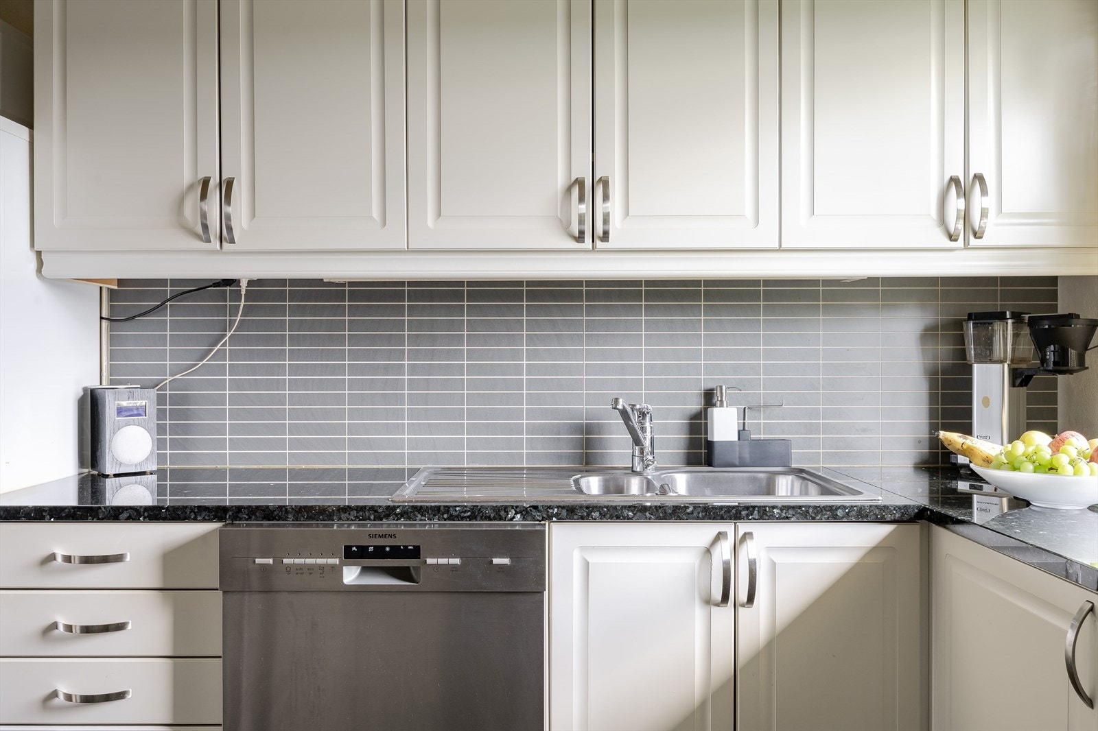 Innredningen har lyse profilerte fronter og påkostet benkeplate av stein med nedfelt oppvaskkum. Praktisk med plater i benkeryggen, belysning under overskapene og sluk i gulv under innredningen. Galleribilde