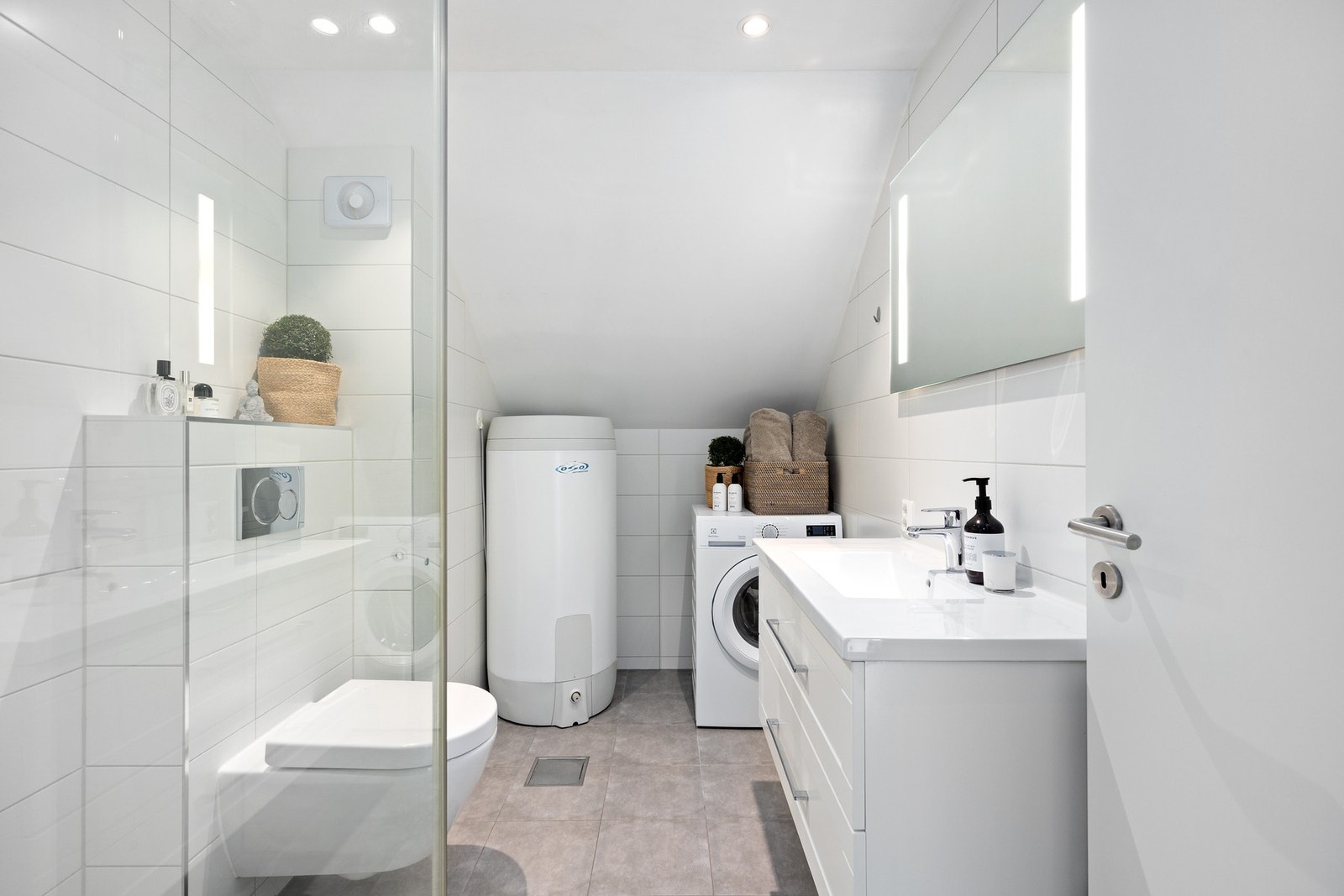 Pent flislagt baderom som ble pusset opp i 2016. Her er det vegghengt wc, servantmøbel med skuffer, veggspeil med belysning, varmtvannsbereder og opplegg for vaskemaskin. Galleribilde